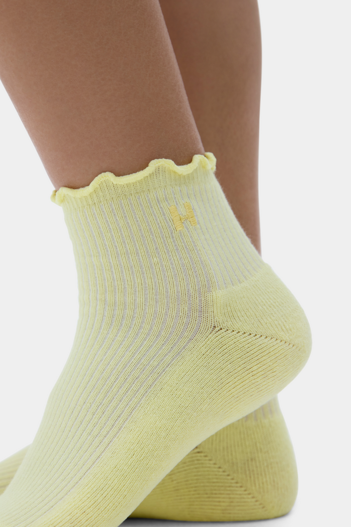 Yellow ankle socks with a scalloped edge and brand logo on a white background