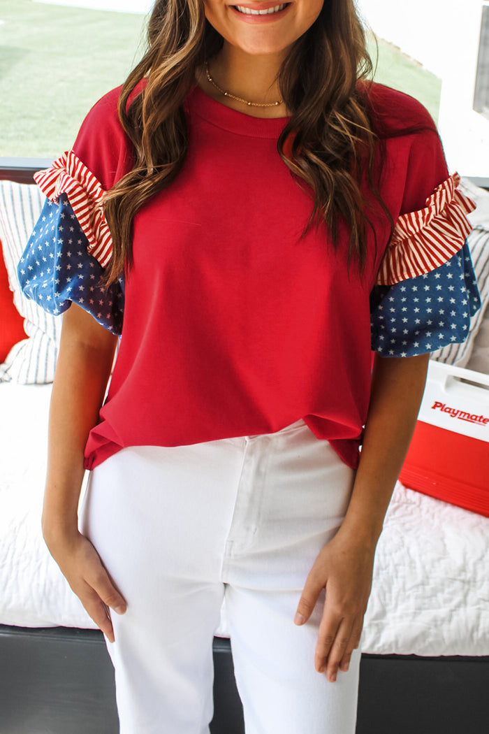 Red stars and stripes puff sleeve top with crew neckline and patriotic details, styled with white pants from The Pink Doxie Boutique.