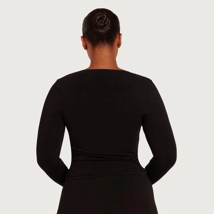 A woman viewed from the back wearing a black long-sleeve top against a light gray studio background.